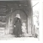 Historická fotografia gazdinej v Zákamennom, stojacej pred dverami chyže spolu s malým dievčatkom; historická fotografia.